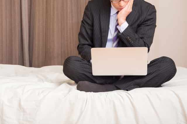 転職エージェントが信用できないと考えている男性がベッドの上でPCを見て考えている