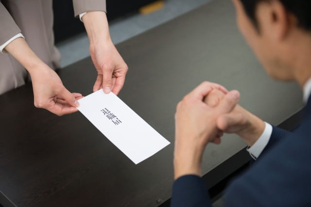 仕事を辞めたいけど言えないスーツを着た女性が勇気を出して退職願を差し出している