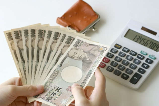 1万円札を手にとって数えて電卓で計算する女性