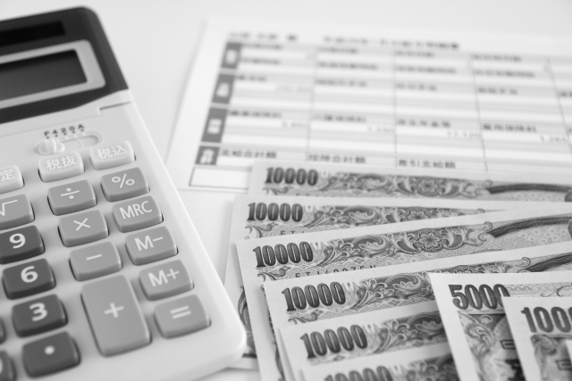 机上に電卓と複数の一万円札、給与明細書が置かれているモノクロの写真