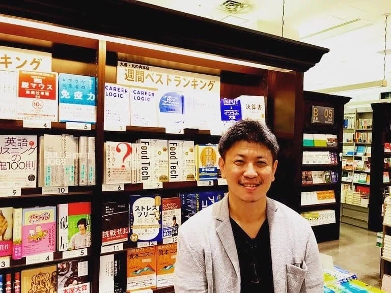 丸善・丸の内本店の週間ベストランキングの棚の前に立つ末永雄大。棚には「キャリアロジック」が1位の位置に平積みされている